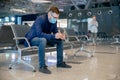 Traveler business man wearing face mask at airport waiting to board plane, using smartphone to check stock quotes market Royalty Free Stock Photo