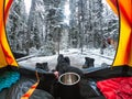 Traveler camping with hand holding cup in a tent with snow in pine forest at national park