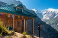 A traveler capturing memories on a smartphone near a traditional wooden mountain homestay in Himachal Pradesh