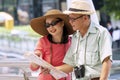 Couple elderly wear hat with luggage, camera and binoculars holding map in hands while walking together in street city. Royalty Free Stock Photo