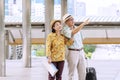 Couple elderly wear hat with luggage holding paper map in hands while walking together in street city. They are using map Royalty Free Stock Photo