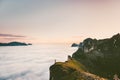 Traveler on the edge cliff mountain above sunset clouds