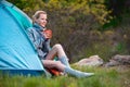 Traveler Girl with a cup of tea resting near a tent against green forest background