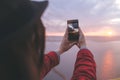 Traveler girl holding phone and taking photo of beautiful evening sky on top of rock mountain. Copy space. Atmospheric moment. Royalty Free Stock Photo