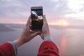 Traveler girl holding phone and taking photo of beautiful evening sky on top of rock mountain. Copy space. Atmospheric moment. Royalty Free Stock Photo