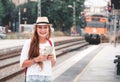 Traveler girl with map, hat and backpack walking train on railway platform.