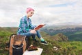 A traveler girl sits in the mountains on the grass and reads a book on the background of epic mountains. The concept of