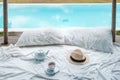 Traveler hat, hot tea cup and teapot on white bed against Beautiful ocean view background, Tourists relaxing in tropical resort Royalty Free Stock Photo