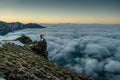 Traveler with hiking sticks standing at the edge of the cliff above clouds during sunrise Royalty Free Stock Photo