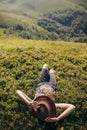 Traveler hipster girl in hat lying on grass in sunny mountains a