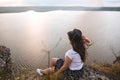 Traveler hipster girl in hat and windy hair sitting on top of rock mountain with wildflowers, looking at beautiful sunset view on Royalty Free Stock Photo