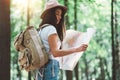 Traveler hipster woman with backpack and hat hold in hands location map and searching directional among trees in forest