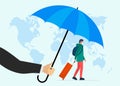 Traveler insurance concept. Agent hand holding umbrella above traveling man with baggage suitcase in protect face mask Royalty Free Stock Photo