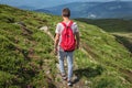 Traveler man with a red backpack, guy lost in the mountains walking along the path afoot,  boy spring summer walk back in nature, Royalty Free Stock Photo