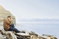 Traveler man sitting on coastline and taking photographs Royalty Free Stock Photo