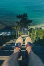 Traveler Man Sitting On Steps Of Stairs Coast Above Sea, View Of Legs. Point Of View Shot