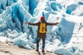 Traveler man with a yellow backpack wearing a red hat standing on a rock on the background of a glacier, mountains and snow. Royalty Free Stock Photo