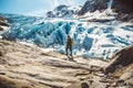 Traveler man with a yellow backpack wearing a red hat standing on a rock on the background of a glacier, mountains and snow. Royalty Free Stock Photo