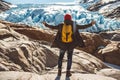 Traveler man with a yellow backpack wearing a red hat standing on a rock on the background of a glacier, mountains and snow. Royalty Free Stock Photo