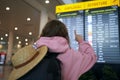 Traveler in pink jacket checks flight times on airport departure board, holiday journey. Festive getaway, woman with