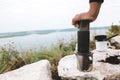 Traveler pressing aeropress on metal mug on cliff at lake, brewing alternative coffee at camping. Making hot drink at picnic Royalty Free Stock Photo