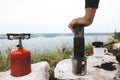 Traveler pressing hot water through coffee in aeropress on cliff at lake, brewing alternative coffee at camping. Making hot drink Royalty Free Stock Photo