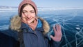 The traveler takes a selfie and waves her hand at the camera of her smartphone. Smiling girl during a trip to the winter Baikal.