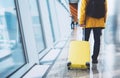 Traveler tourist in bright jacket with yellow suitcase backpack at airport on background large window blue sky, man waiting