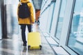 Traveler tourist in bright jacket with yellow suitcase backpack at airport on background large window blue sky, man waiting Royalty Free Stock Photo