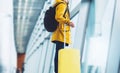 Traveler tourist in bright jacket with yellow suitcase backpack at airport on background large window blue sky, man waiting Royalty Free Stock Photo