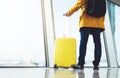 Traveler tourist hold yellow suitcase backpack is standing at airport on background large window, man in bright jacket waiting Royalty Free Stock Photo