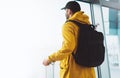 Traveler tourist with yellow backpack is standing at airport on background large window, man in bright jacket waiting in departure Royalty Free Stock Photo