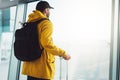 Traveler tourist with yellow backpack is standing at airport on background large window, man in bright jacket waiting in departure Royalty Free Stock Photo