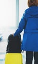 Traveler tourist with yellow suitcase backpack is standing at airport on background large window, girl in bright jacket waiting Royalty Free Stock Photo