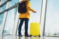 Traveler tourist with yellow suitcase backpack is standing at airport on background large window, man in bright jacket waiting Royalty Free Stock Photo