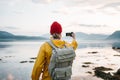 Traveler wearing yellow raincoat taking photo by smartphone fantastic nord landscape while traveling scandinavia