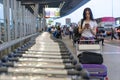 Traveler woman in airport terminal using mobile smartphone with luggage and bag on airport trolley cart with busy airport