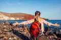 Traveler woman with backpack relaxing raising arms on Red beach on Santorini island, Greece enjoying landscape. Royalty Free Stock Photo