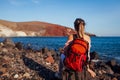 Traveler woman with backpack relaxing on Red beach on Santorini island, Greece enjoying landscape. Royalty Free Stock Photo