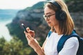 Traveler woman with hipser glasses holds mobile phone in hands and selects music for headphones via Internet technology to enjoy Royalty Free Stock Photo