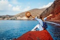 Traveler woman relaxing raising arms on rock on Red beach on Santorini island, Greece. Traveling and vacation Royalty Free Stock Photo