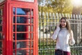 Traveler woman talks on her cellphone next to a red telephone booth in London, UK Royalty Free Stock Photo