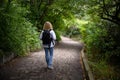 Traveler woman walks away in forest. Lonely girl hiker is alone on path in dark woods