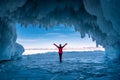 Traveler woman wear red clothes and raising arm standing on frozen water in ice cave at Lake Baikal, Siberia, Russia