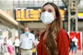 Traveler woman wearing KN95 FFP2 face mask at the airport. Young caucasian woman with behind timetables of departures arrivals