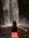 Traveler woman wearing pink dress at waterfall. Excited woman raising arms in front of waterfall. Travel lifestyle. View from back Royalty Free Stock Photo