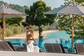 Traveler woman in white dress and hat sitting on sun lounger near swimming pool Royalty Free Stock Photo