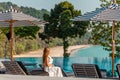 Traveler woman in white dress and hat sitting on sun lounger near swimming pool Royalty Free Stock Photo