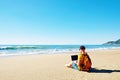 Muscle guy wearing surfer outfit, blue shorts and yellow t-shirt, working on holiday with laptop on an empty beach Royalty Free Stock Photo