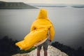 Traveler in yellow raincoat standing on cliff and looking at lake in rainy windy day. Wanderlust and travel concept. Hipster man Royalty Free Stock Photo